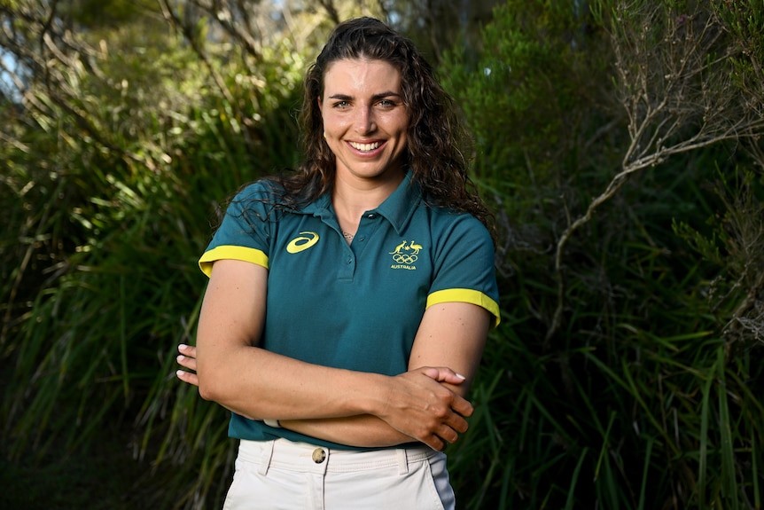Jessica Fox, crossing her arms, smiling, wearing and Australia Olympic polo shirt, standing among trees