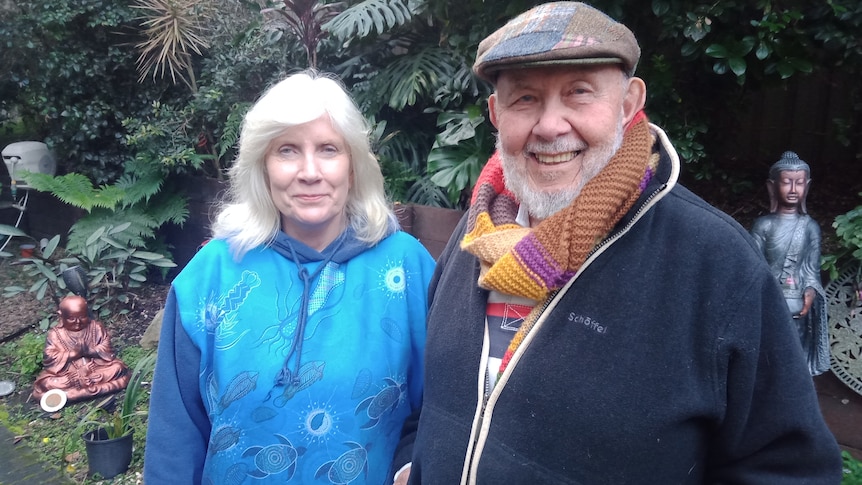 two people, smiling at the camera, standing in their garden.