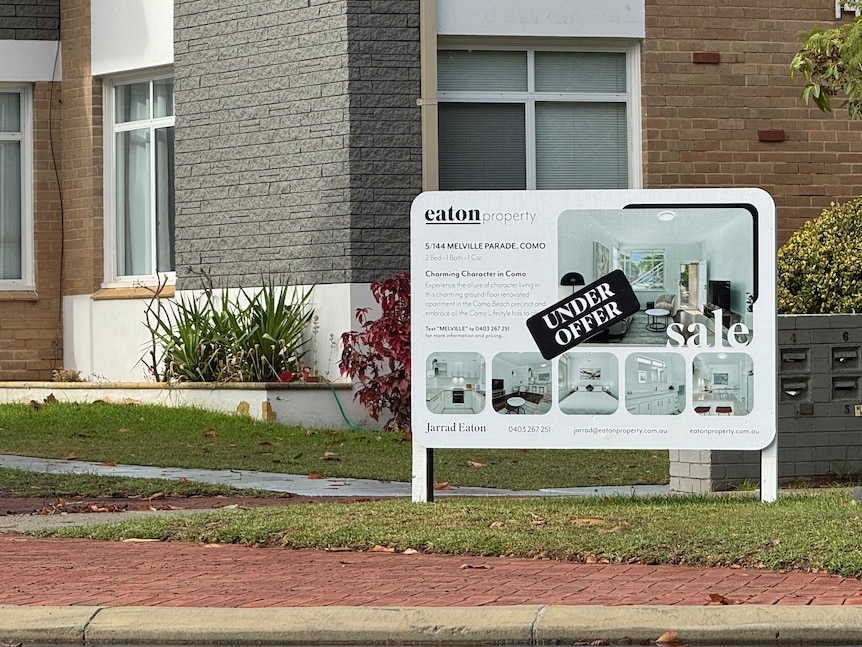 a white sign with "under offer' is standing infront of a block of units