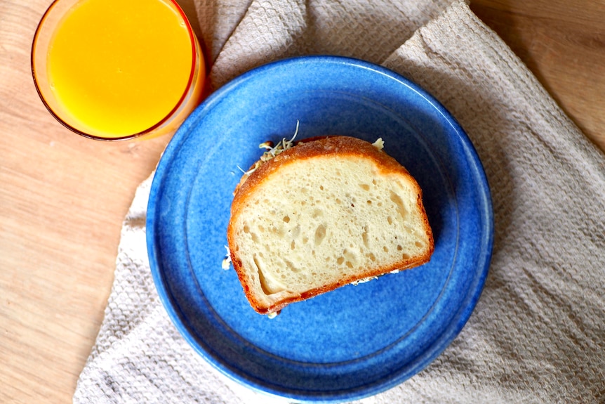 Sandwich made with homemade bread on a blue plate, a glass of orange juice beside it.