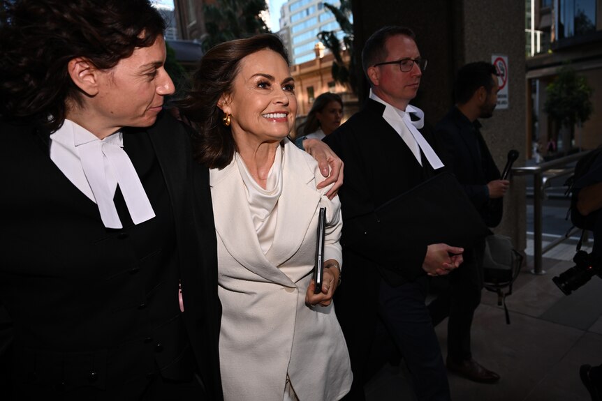 A woman in a white suit smiles, in the arms of a lawyer.