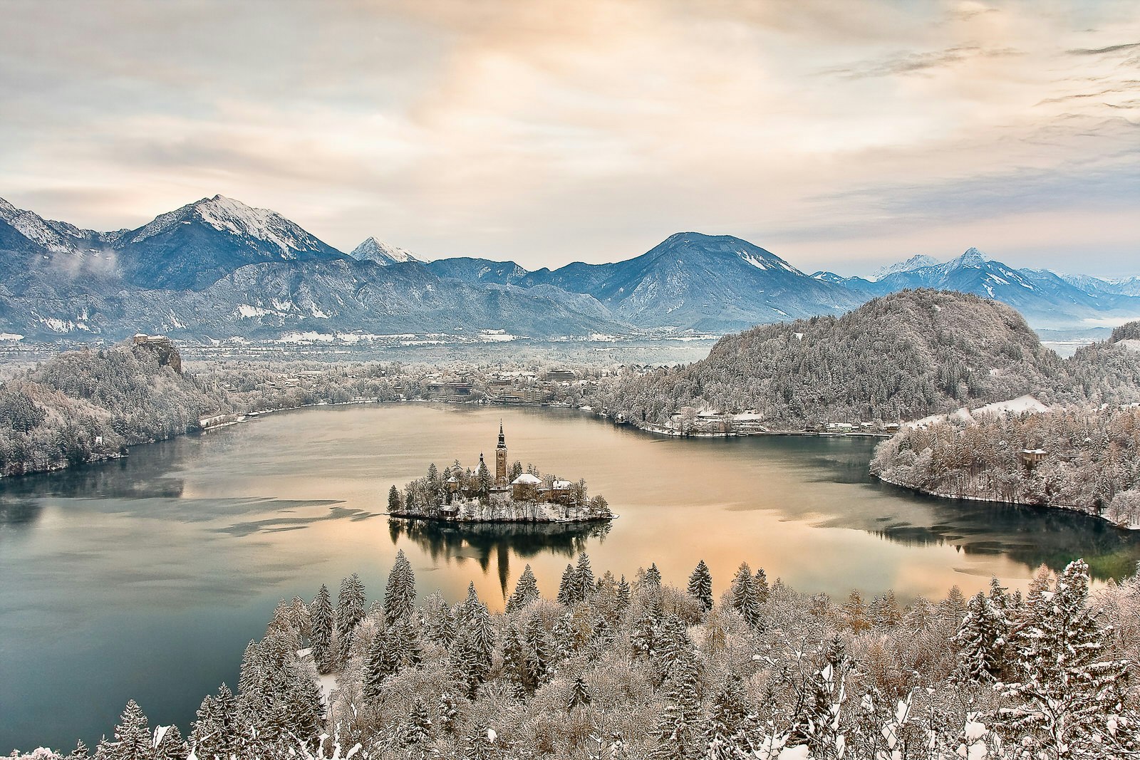 A stunning aerial shot of a lake with a church on an island in the middle. The woodland and hills around the lake are icy with some snow