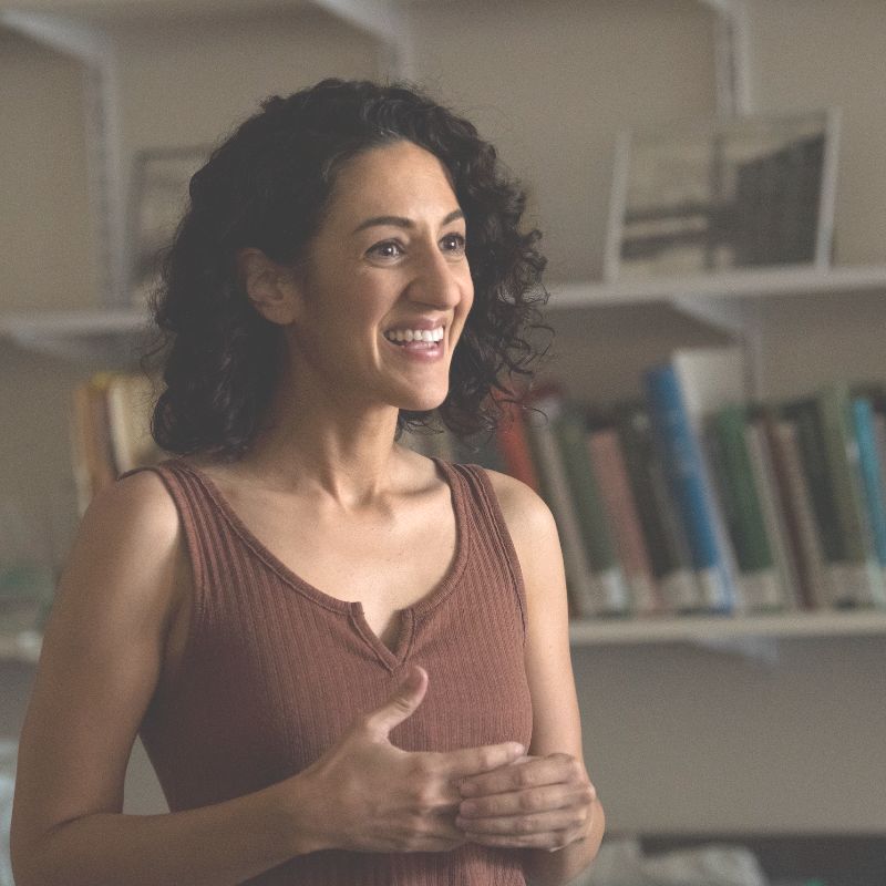 Marina LaForgia smiles looking off camera. She has dark, shoulder length curly hair and is wearing a brown tank top.