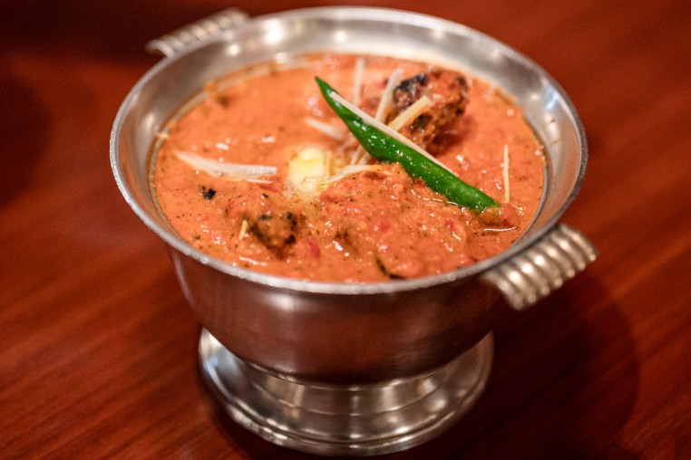 A dish of butter chicken is presented on a dining table in a silver chalice