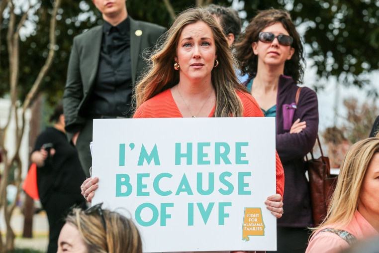 A woman holds a sign that reads "I'm Here Because of IVF"