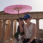 Tourists with an umbrella walk in front of the Parthenon at the ancient Acropolis in Athens