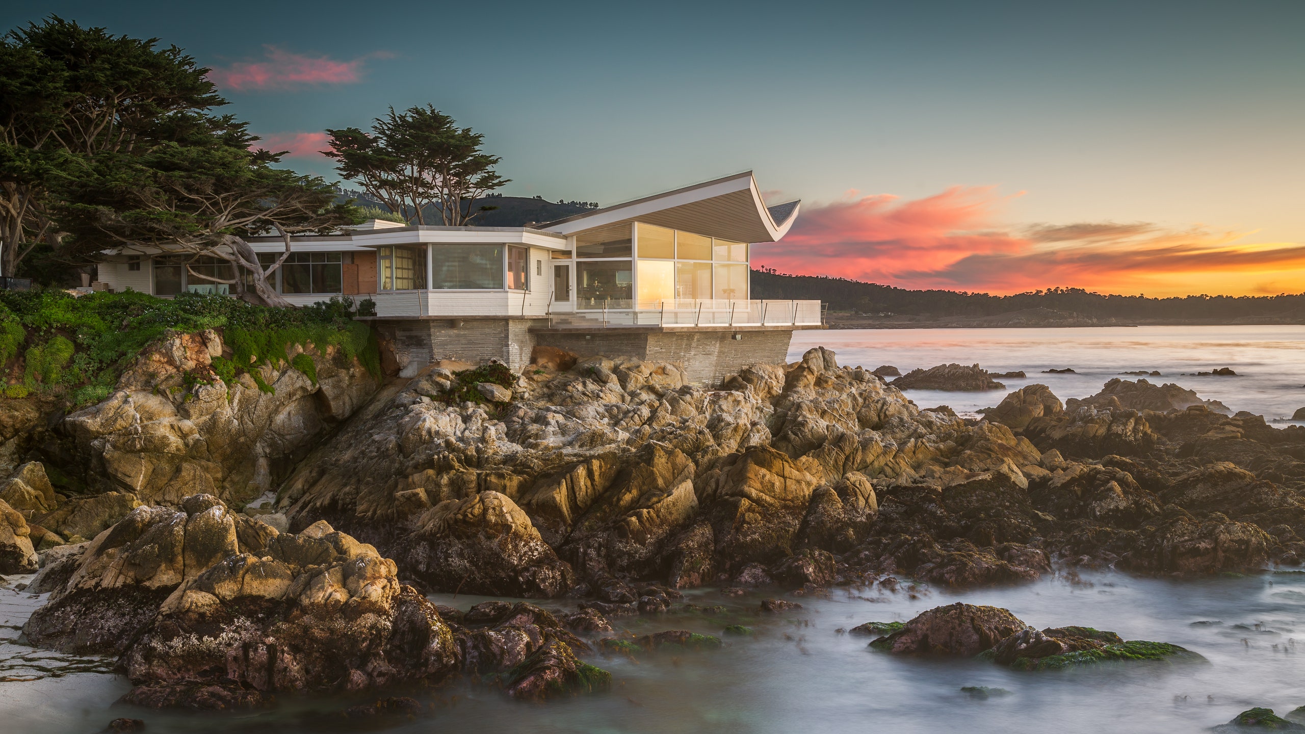 The Butterfly House sits on the rocks as the Pacific ocean waves crash on the rocky beach coast in Carmel California.