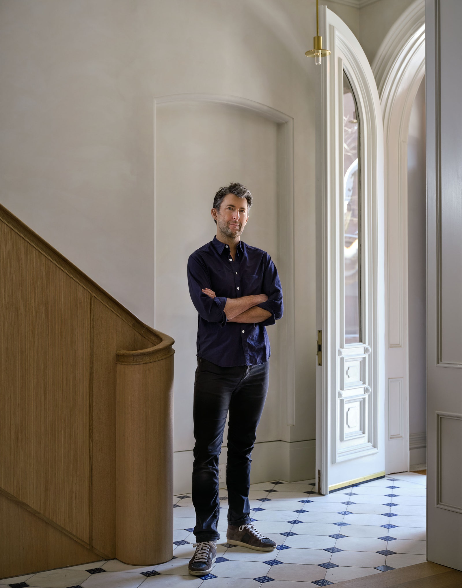 Oliver Freunlich standing on tiled floor by wooden banister arched white door open to the right