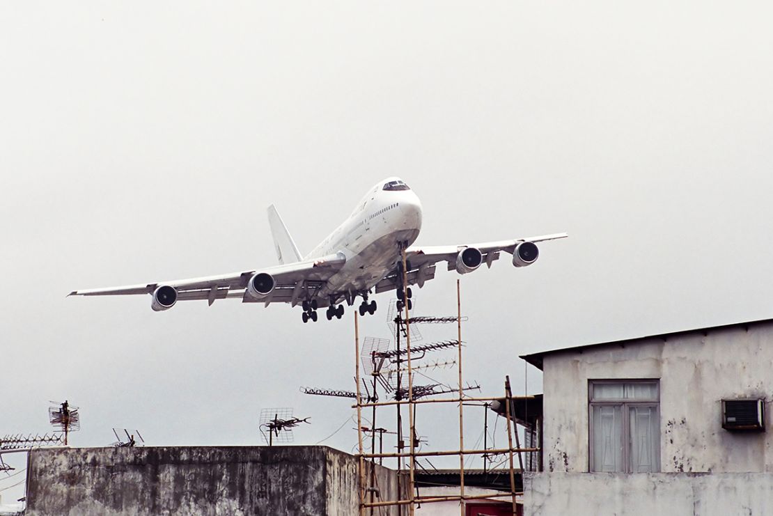 Not a common airport sight elsewhere -- a plane flying right above bamboo scaffolding and TV antenna. 