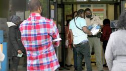 In this Thursday, April 23, 2020, photo a Pulaski County (Arkansas) Sheriff's officer gives out numbers as people wait in line at the Arkansas Workforce Center, in Little Rock. Payouts from the state's Unemployment Insurance Trust Fund soared last week to nearly $17.6 million.