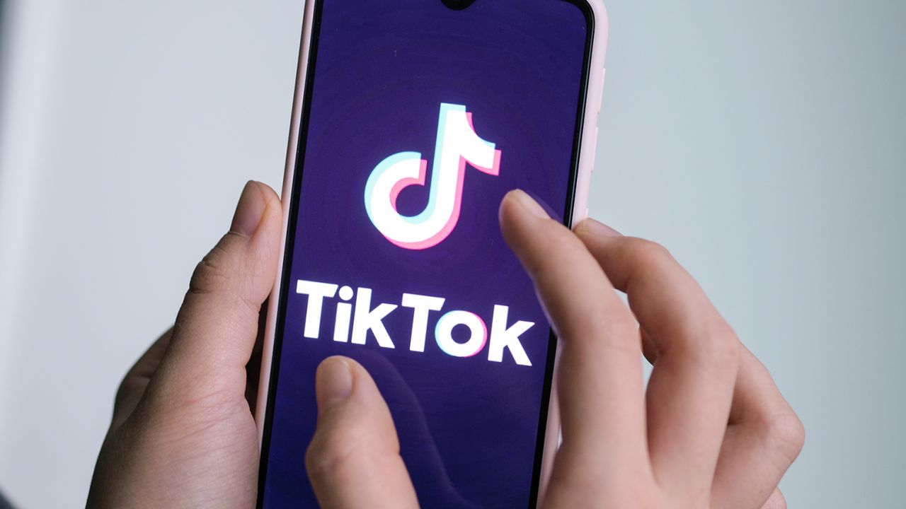 A girl is holding her smartphone with the logo of the short video app TikTok in her hands. 