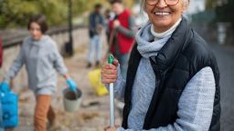 Happy senior woman volunteer with team cleaning up street, community service concept