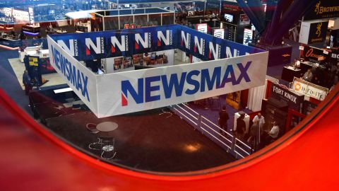 FILE PHOTO: A Newsmax booth broadcasts as attendees try out the guns on display at the National Rifle Association (NRA) annual convention in Houston, Texas, U.S. May 29, 2022. Picture taken through glass. REUTERS/Callaghan O'Hare/File Photo