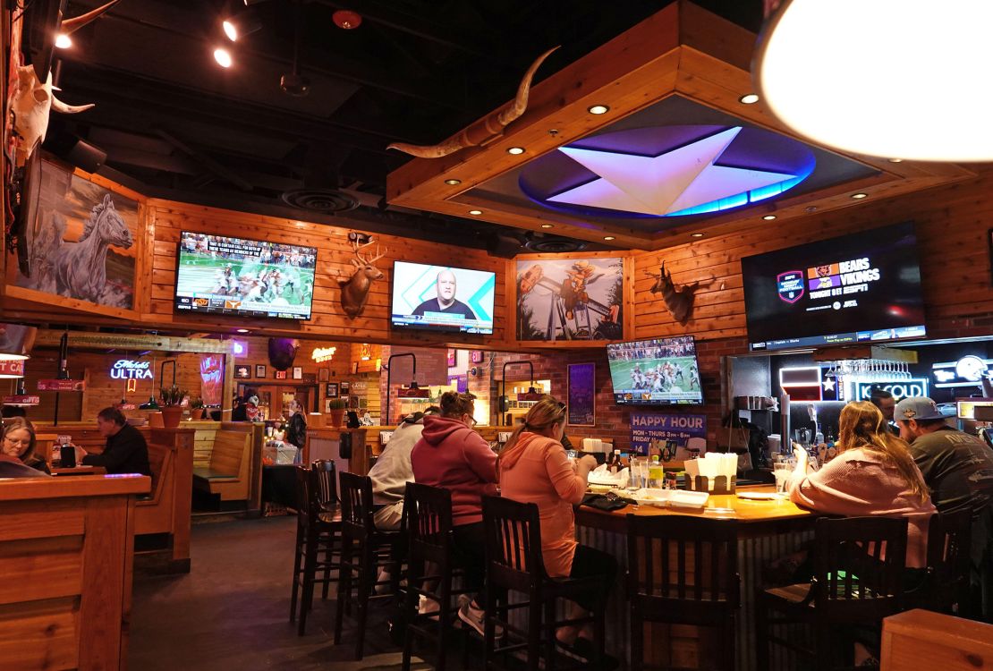 Patrons sit at a bar and watch sports at a Texas Roadhouse restaurant in November 2023.