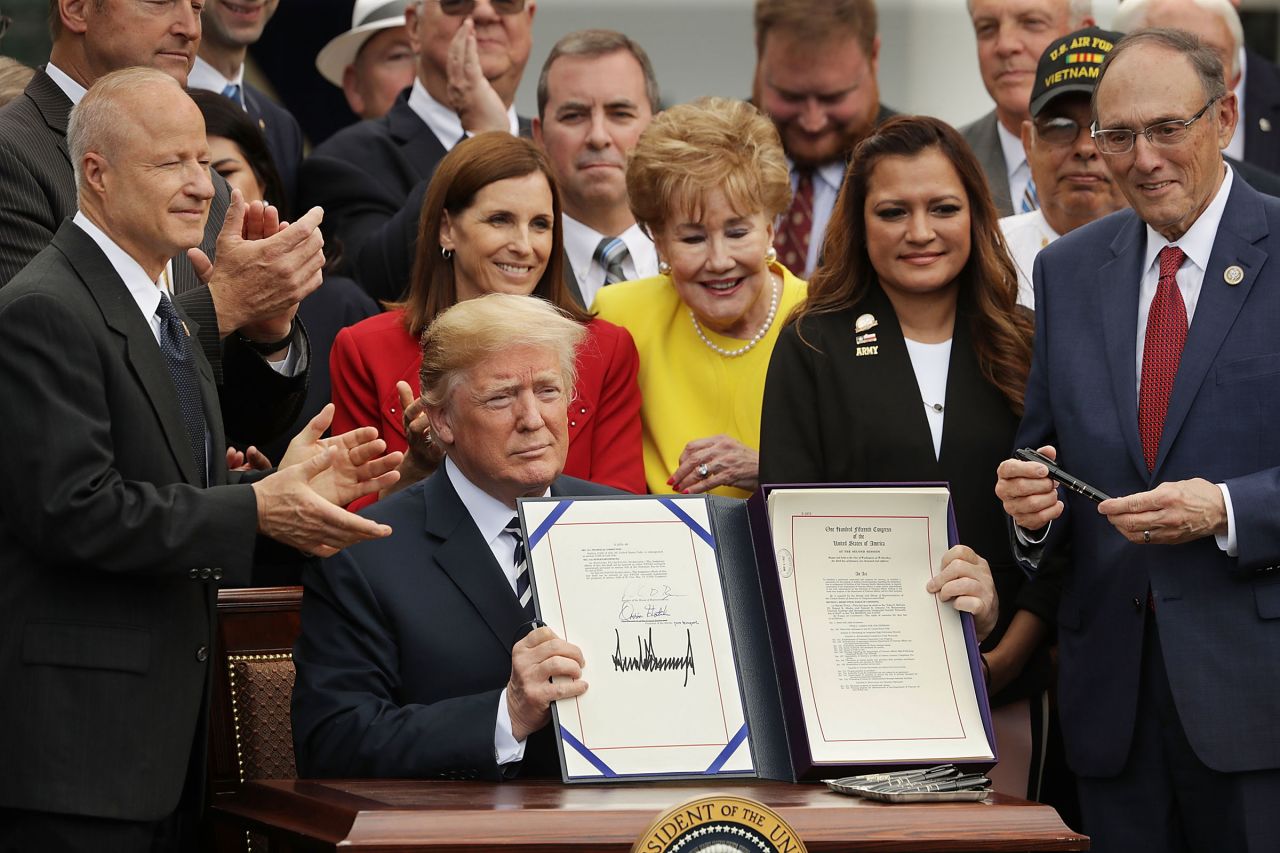 In this 2018 photo, then-President Donald Trump holds up the Veterans Affairs Mission Act he signed during a ceremony with members of Congress, including House Veterans Affairs Committee Chairman Phil Roe and veterans in the Rose Garden at the White House in Washington, DC. The new law continued funding for the Veterans Choice Program for an additional year.