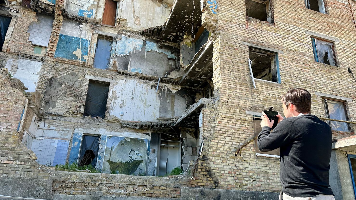 French tourist Jean-Baptiste takes a photo of a Banksy painting on the wall of a house destroyed by Russians in the suburbs of Kyiv