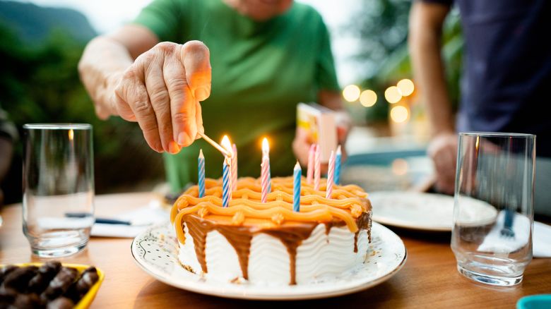 Close-up of a senior woman lighting candles on a cake during her birthday party outside on a patio at home