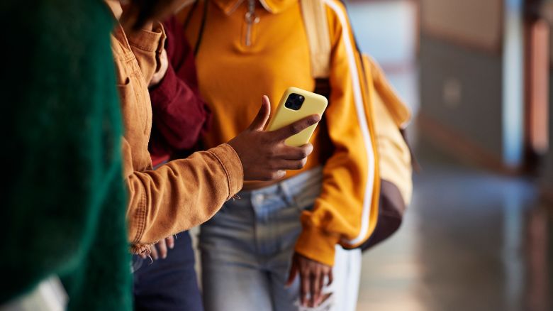 Midsection of friends sharing smart phone in hallway at high school