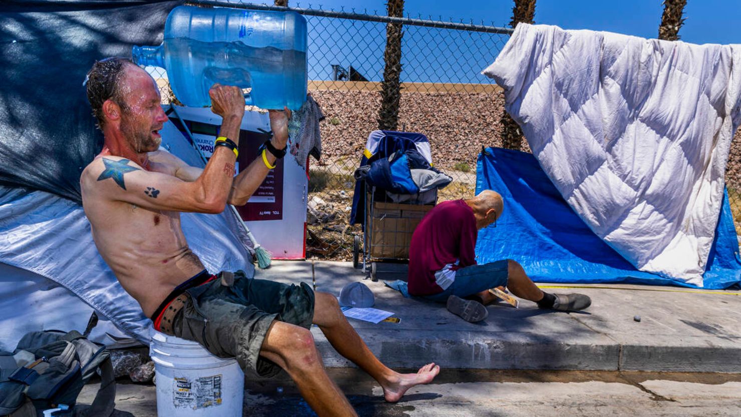 Milton John Scott III, who is unhoused, pours a jug of water on his head to escape the heat and wash up at his shelter in Las Vegas, Nevada on June 5.