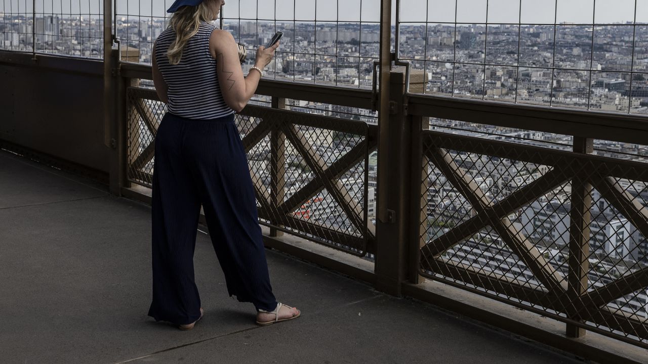 A woman looks at her phone at the Eiffel Tower in Paris, on June 26, 2024.