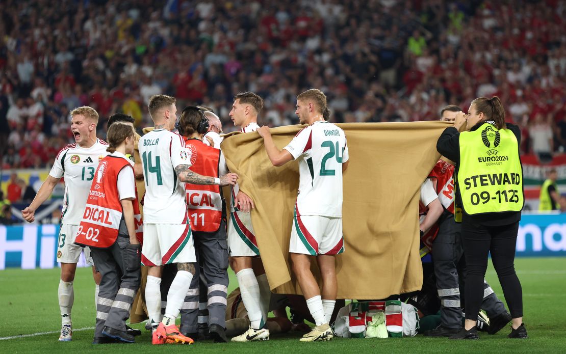 Hungary players hold up blankets as they assist medical staff by covering up Varga as he receives medical attention.