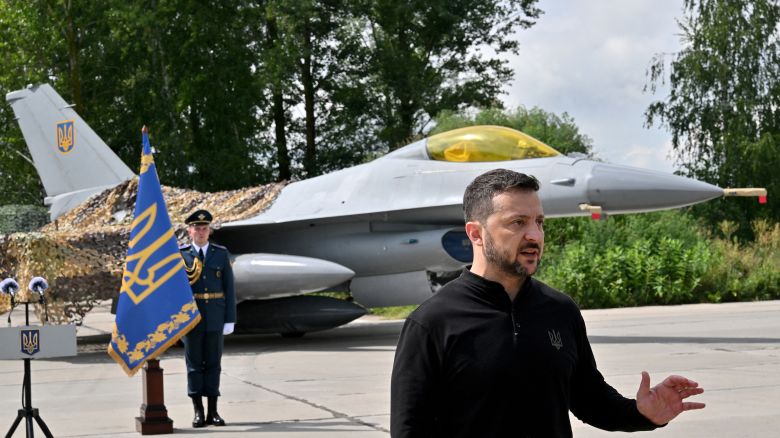 Ukraine's President Volodymyr Zelensky gestures as he speaks to media representatives while standing in front of an F16 fighter jet during Ukrainian Air Forces Day at an undisclosed location on August 4, 2024. Ukraine has received its first batch of US-made F16 fighter jets, Ukrainian President Volodymyr Zelensky said, showing journalists several aircraft that Kyiv hopes will help beat back Russian forces.