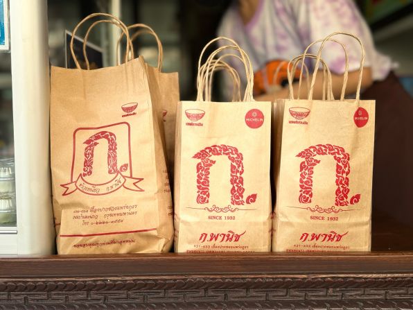 Takeaway bags at K Panich line the busy counter, where delivery drivers await orders on a busy weekday morning.