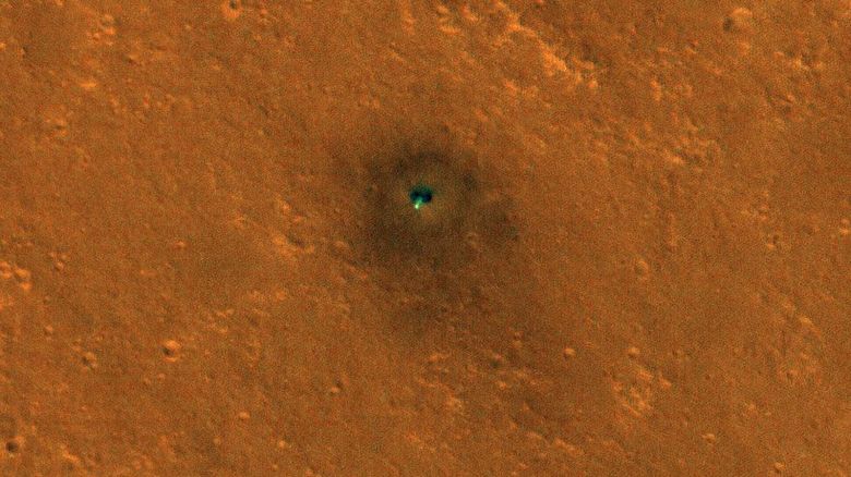 NASA's InSight spacecraft and its recently deployed Wind and Thermal Shield were imaged on Mars on Feb. 4, 2019, by the HiRISE camera aboard NASA's Mars Reconnaissance Orbiter. On Feb. 2, 2019, InSight's robotic arm placed the special shield over its seismometer on the Martian surface to protect the instrument from wind and extreme temperatures. The green object in this image is the InSight lander; the white dot just below it is the shield, which is especially bright and reflective. The shield is a little less than 6 feet (1.8 meters) away from the lander. The dark circles on either side of the lander are its solar panels. The total width of the lander with both panels open is 19 feet, 8 inches (6 meters).