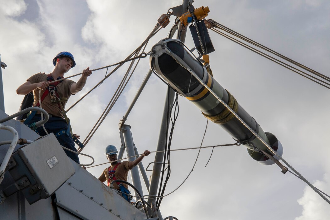 STG3 Josiah Kirchofer, left, and STG2 Pierre Ducasse hoist an Mark 54 torpedo aboard USS Spruance (DDG 111).