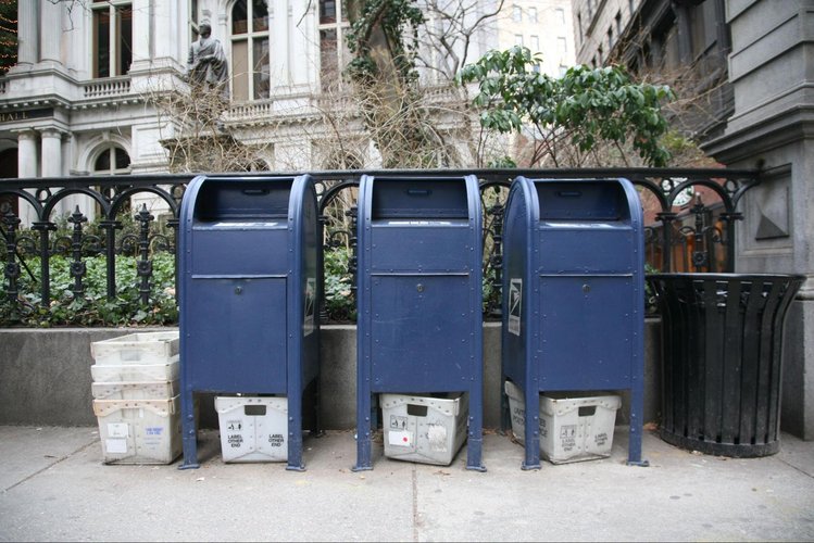 Photo of three blue postal mail boxes on a sidewalk.