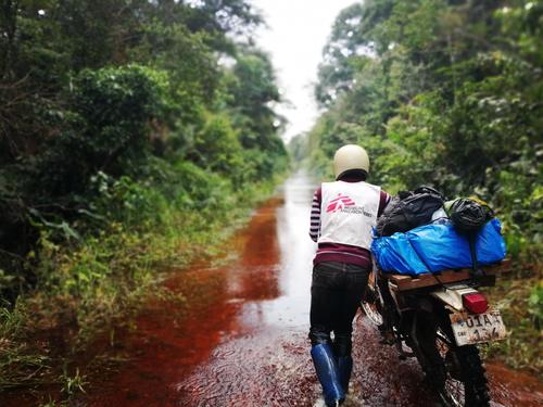 A biker pushes his motorbike loaded with medical cargo in his way to Lokula health post over a flooded road.