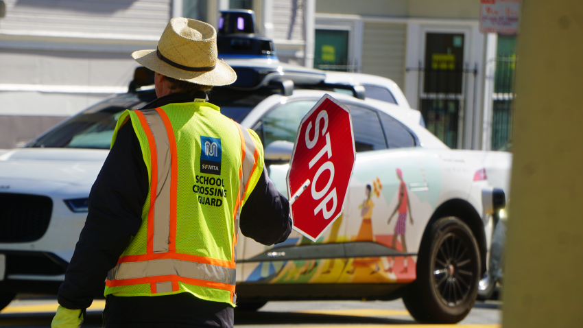 A San Francisco crossing guard walks into the crosswalk as a Waymo driverless vehicle approaches.