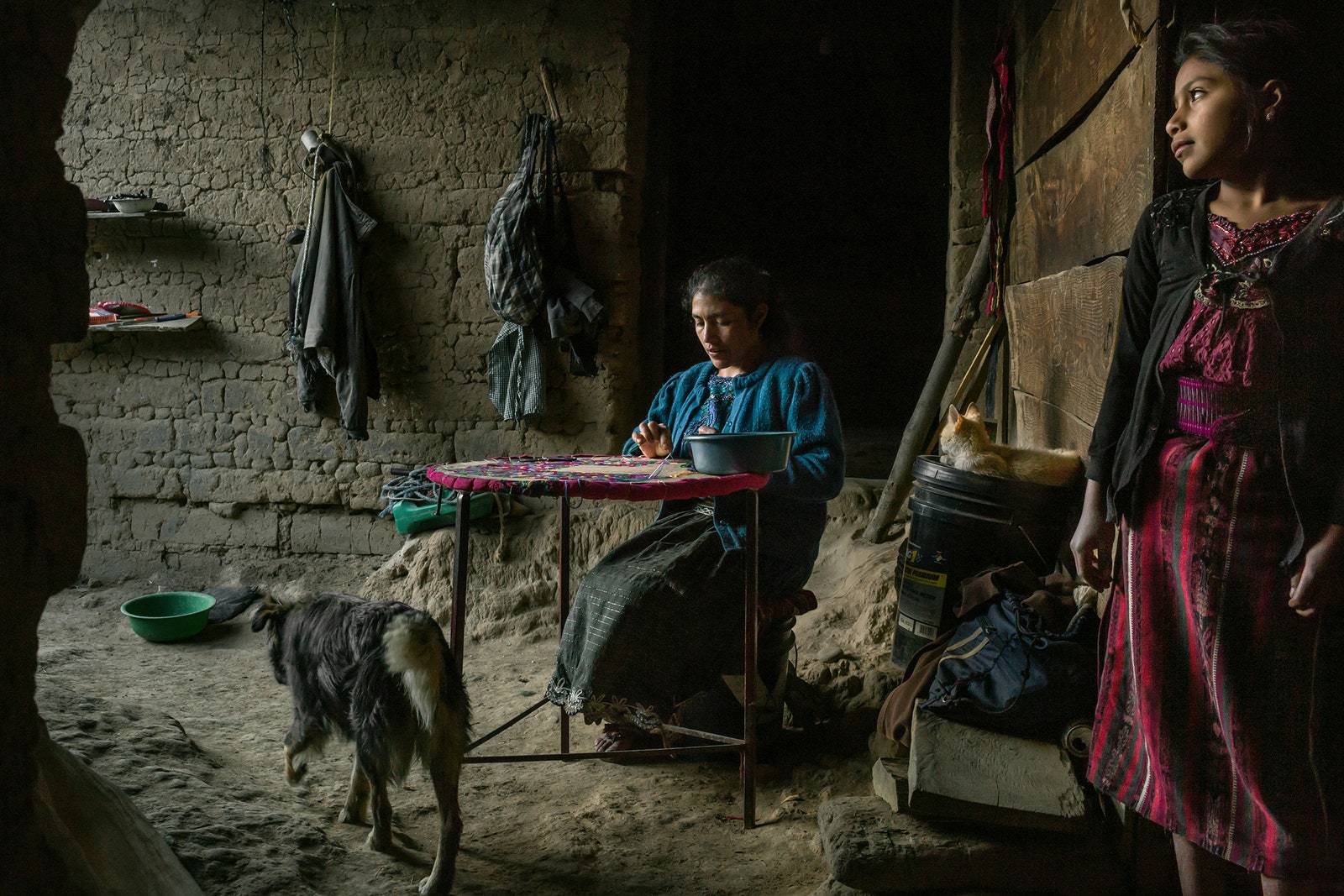 A woman weaves a sweater next to her daughter at home.