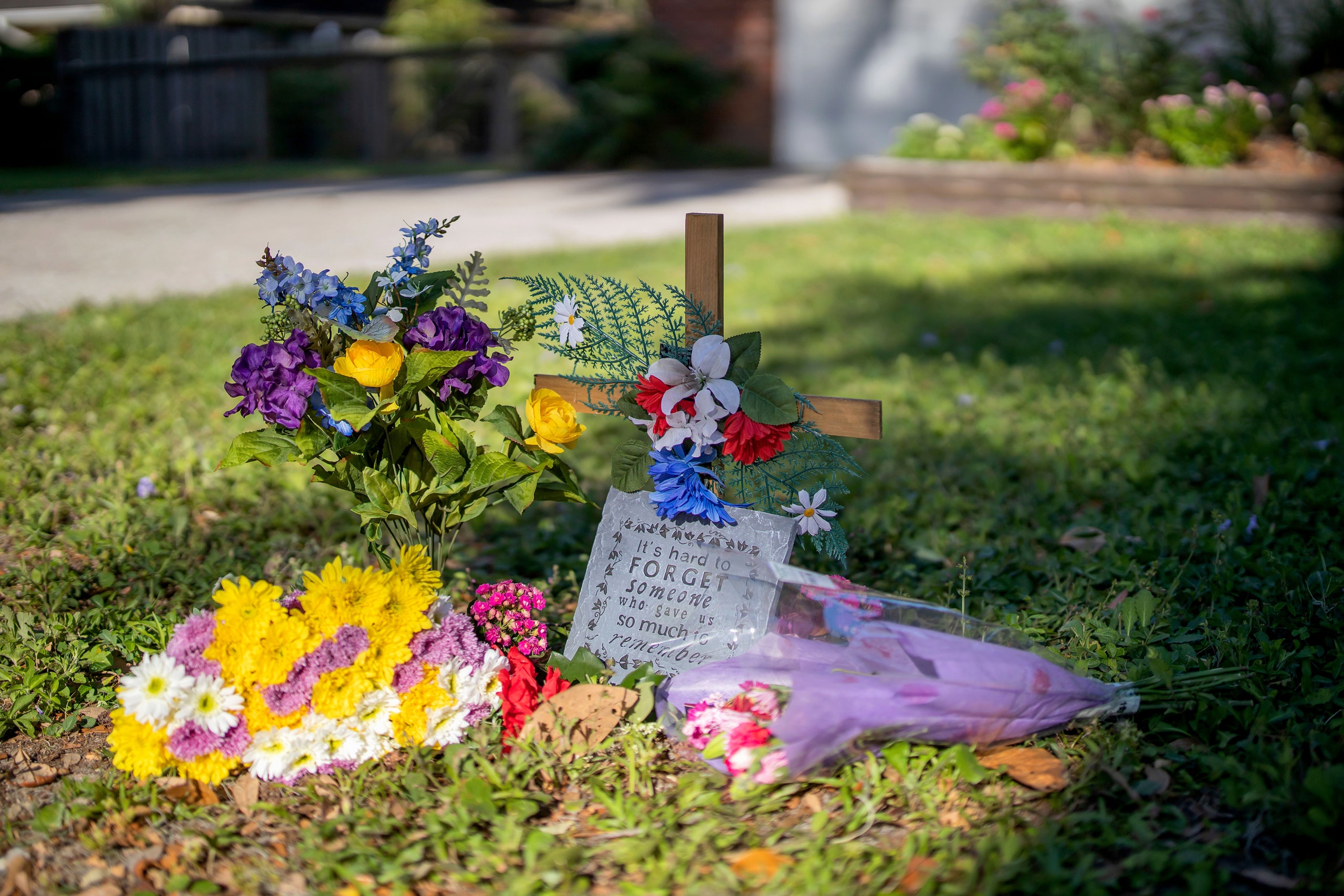 A cross with flowers sits in a front yard.