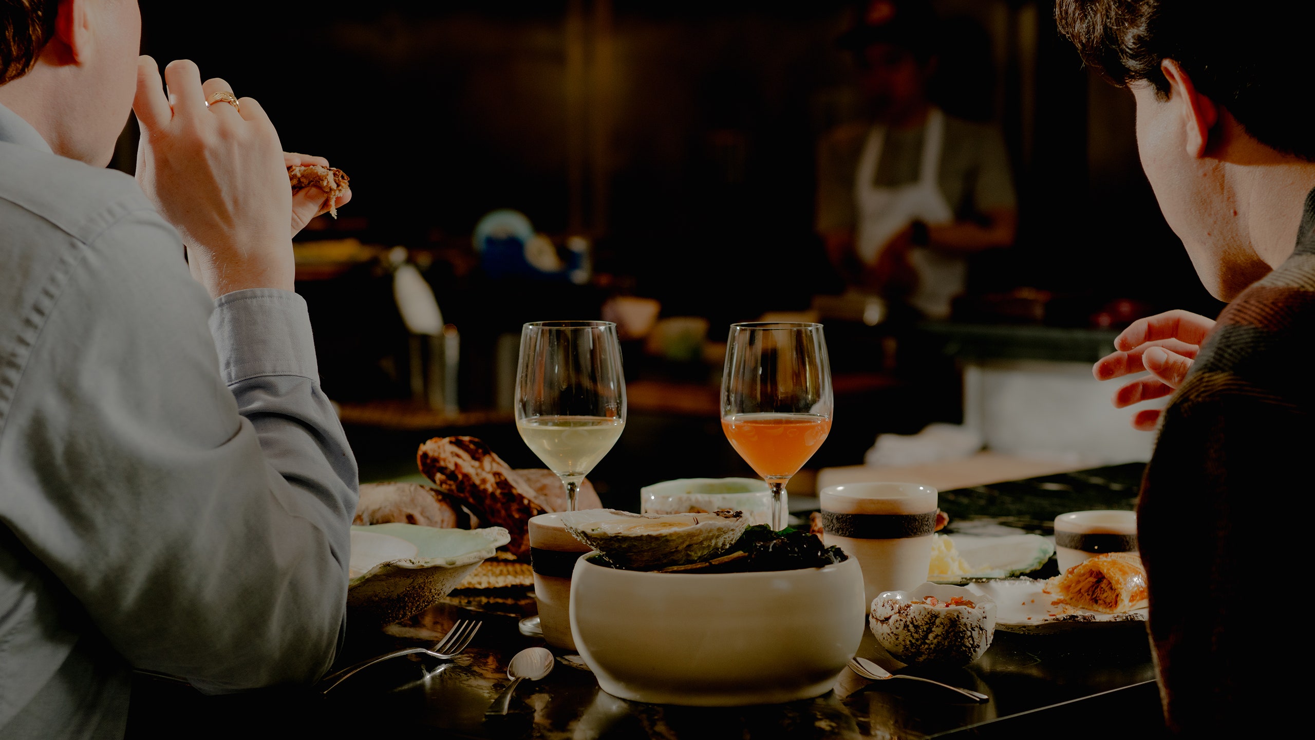 Two people at a table with food and wine.