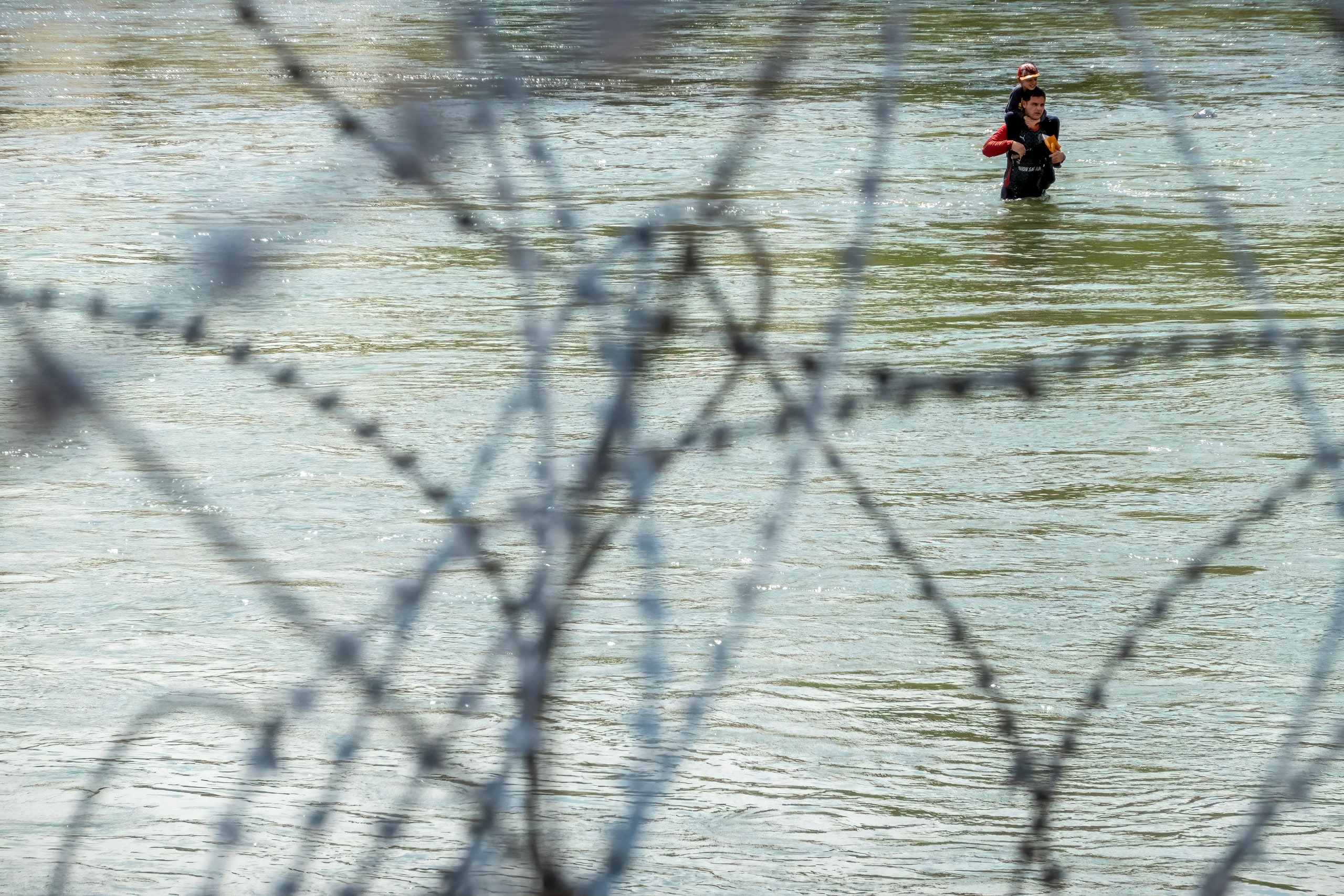 A photo of two people wading through a river as seen through a mess of wires.