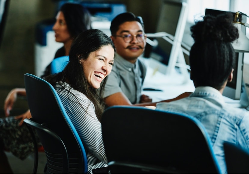 Young woman sitting at desk talking with colleagues