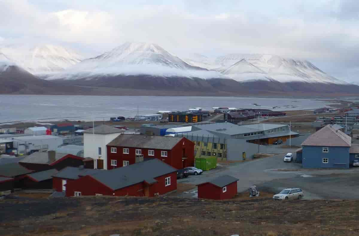 Foto av bygninger på Svalbard med fjord og bredekte fjell i bakgrunnen.