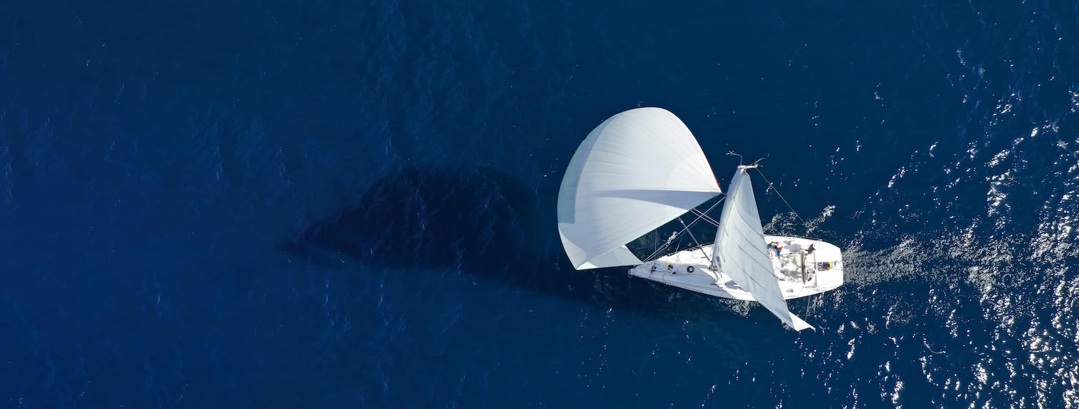 En moderne, bermudarigget seilbåt med storseil (sneiseil) og spinnaker i medvind (lens)