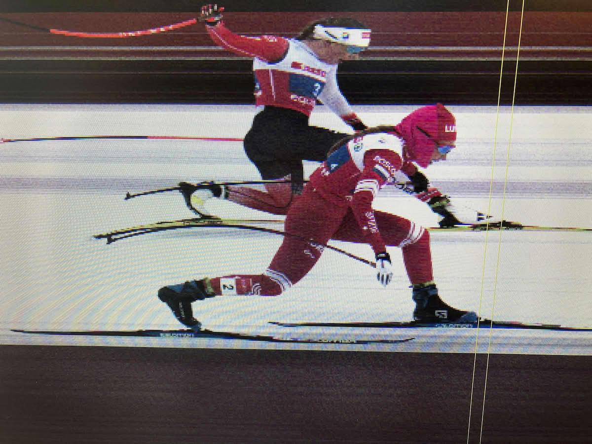 Foto av skjerm som viser målfoto Bekisjeva er nærmest kamera, Heggen er delvis skjult bak henne. På skjermen er det lagt på to gule linjer som viser at tuppen av Heggens skisko er først over målstreken.