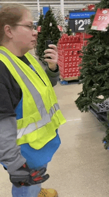 a woman in a yellow vest is looking at a christmas tree