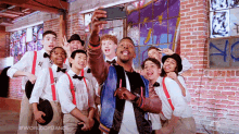 a group of young men are posing for a selfie in front of a brick wall with graffiti on it