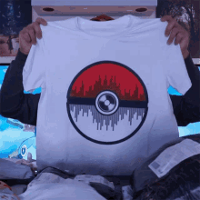 a person is holding up a white t-shirt with a pokeball design on it