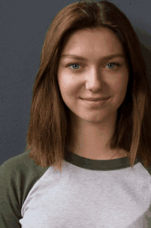 a woman with brown hair and blue eyes wearing a green and white shirt