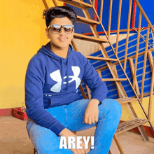 a young man wearing sunglasses and a blue under armour hoodie sits on a wooden staircase with the caption arey