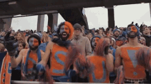 a group of people are standing in a stadium wearing orange and blue shirts with the letter s painted on them .