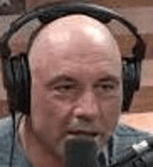 a bald man wearing headphones and a microphone is talking into a microphone .