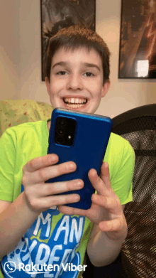 a boy wearing a green shirt with the word man on it holds a blue cell phone