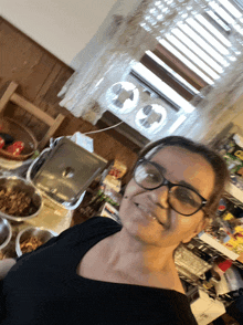 a woman wearing glasses is standing in front of a window with two fans on it