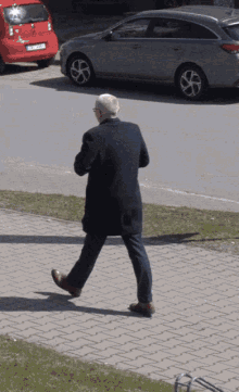 a man in a suit walks down a sidewalk in front of a car with a license plate that starts with the letter n